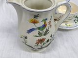 a small pitcher with a bird on it next to a spoon and spoon rest