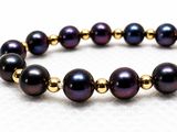 a close up of a bracelet with black pearls and gold beads