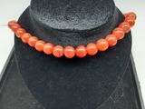 un gros plan d'un collier porté par un mannequin, orné d'une perle orange