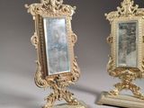 pair of ornate gold framed mirrors on stands on a gray background
