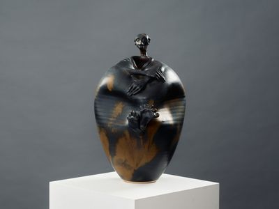 un vase noir et marron posé sur un socle blanc