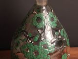 a glass bottle with green flowers on it sitting on a table