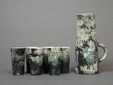 five cups and a jug sitting next to each other on a table