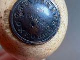 a hand holding a wooden object with a metal button on it