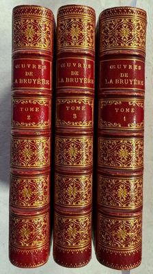 trois livres rouges et dorés posés sur une surface blanche