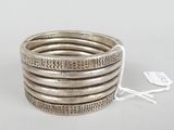 a close up of a stack of silver bracelets on a white surface