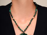 un gros plan d'une femme portant un collier orné d'un pendentif vert