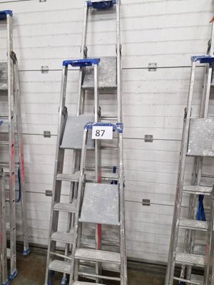 Plusieurs échelles sont alignées contre un mur blanc dans un entrepôt