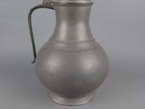 an old silver pitcher sitting on top of a gray table