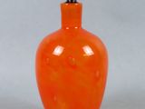 une bouteille en verre orange avec un bouchon noir, posée sur une surface blanche