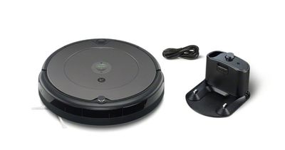 un aspirateur robot noir posé à côté d'un chargeur sur une surface blanche