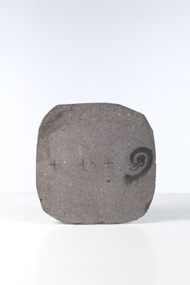 une pierre sur laquelle est gravé un visage, posée sur une surface blanche