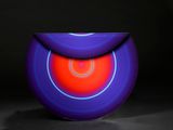 un vase violet et rouge posé sur une surface noire, avec un livre en arrière-plan