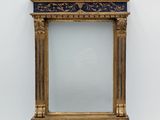 un miroir orné de motifs dorés et bleus, avec un cadre doré, accroché à un mur blanc