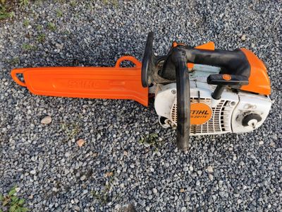 an orange chainsaw sitting on the ground next to some gravel