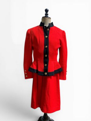une veste et une jupe rouges, ornées de passementerie noire et de boutons, présentées sur un mannequin