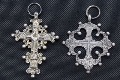 two silver cross pendants on a black background