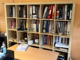a desk with a chair and a book shelf in the corner