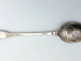 une cuillère en argent avec un manche en argent posée sur une surface blanche