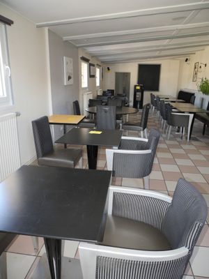 Des tables et des chaises sont alignées dans une pièce au sol carrelé.