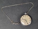 a silver pocket watch on a chain on a black surface