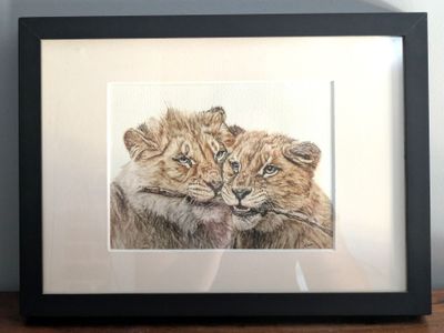 painting of a couple of lions in a black frame on a wooden table