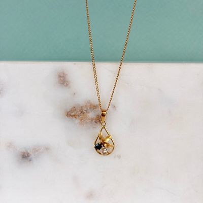 un collier plaqué or orné d'un diamant noir posé sur une surface en marbre