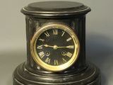 a small black clock with roman numerals on it