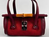 hand holding a red purse with a wooden handle on a white surface