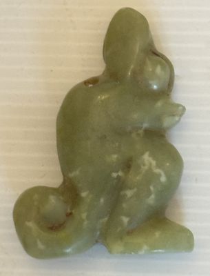 une statue verte représentant une grenouille assise sur une surface blanche