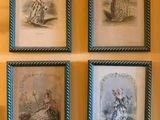four framed pictures of women in dresses and hats on a wall
