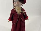 une petite poupée qui porte une robe rouge et un chapeau