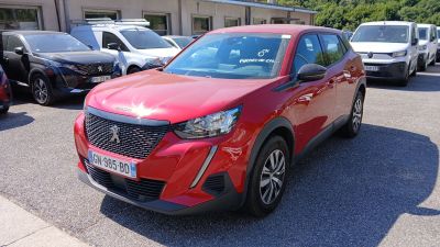 La voiture rouge est garée sur un parking, avec d'autres voitures en arrière-plan.