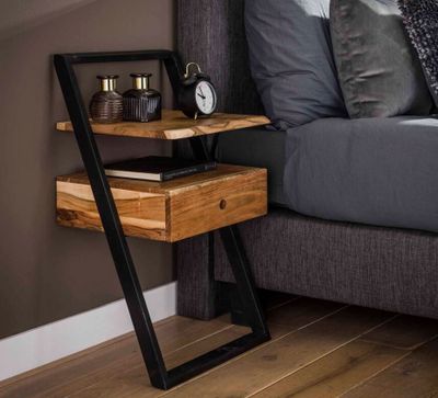 une table en bois sur laquelle se trouve une horloge, à côté d'un lit