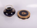 un vase noir et un couvercle doré posés sur une surface blanche
