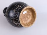 a black vase with a brown lid sitting on a white surface