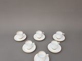 un service de six tasses à café blanches avec leurs soucoupes, posé sur un support gris