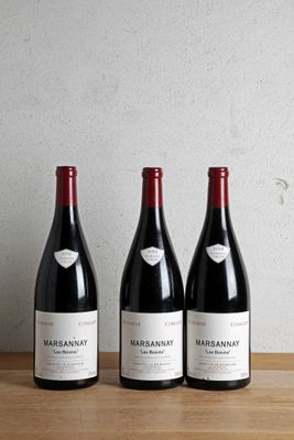 trois bouteilles de vin sont posées sur une table en bois devant un mur