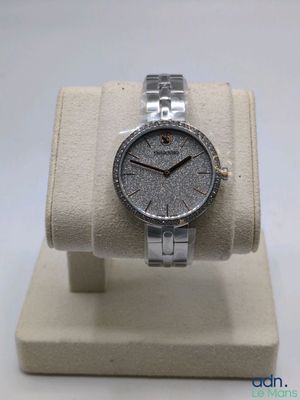 la montre est posée sur un présentoir, sur une surface blanche