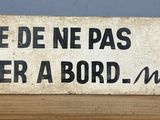 un panneau posé sur un support en bois sur lequel on peut lire « Prére de ne pas monter à bord » Morel