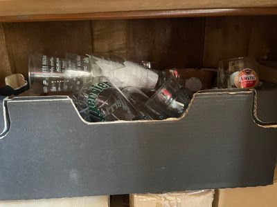 bottles and cans are in a bin on a shelf in a kitchen