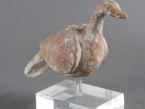 statue d'un canard posée sur un socle transparent, posée à son tour sur une surface grise
