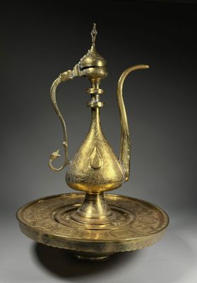 une théière ancienne en laiton posée sur une soucoupe, munie d'une anse