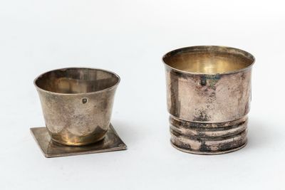 a silver cup and saucer sitting on a white surface