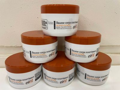 six pots de beurre corporel posés sur un plan de travail blanc