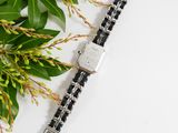 a close up of a watch on a white surface next to a plant