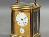 a gold clock with a handle on a gray surface