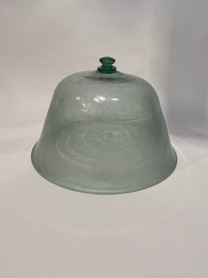 une cloche en verre avec un haut vert posée sur une surface blanche