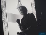 black and white photograph of a woman holding a sign in front of a picture of the eiffel tower
