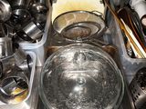 Des casseroles et des poêles sont posées sur un plan de travail de cuisine, à côté d'autres casseroles et poêles.